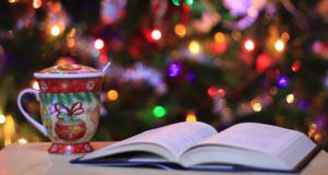 book with holiday mug of cocoa in front of a christmas tree