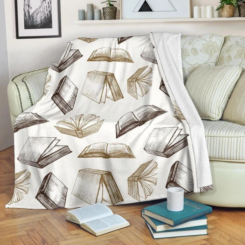 Photo of a blanket draped over a sofa with illustrations of books that seem to have fallen down, as they are all half open. The illustrations are in tones of gray and bronze