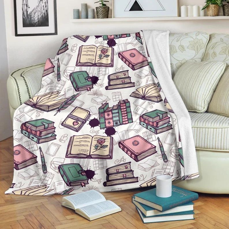 Photo of a blanket draped over a sofa, with illustrations of stacks of books, open books, and books placed next to each other on it, the books have pastel colours like pink and green and the pages are yellowed